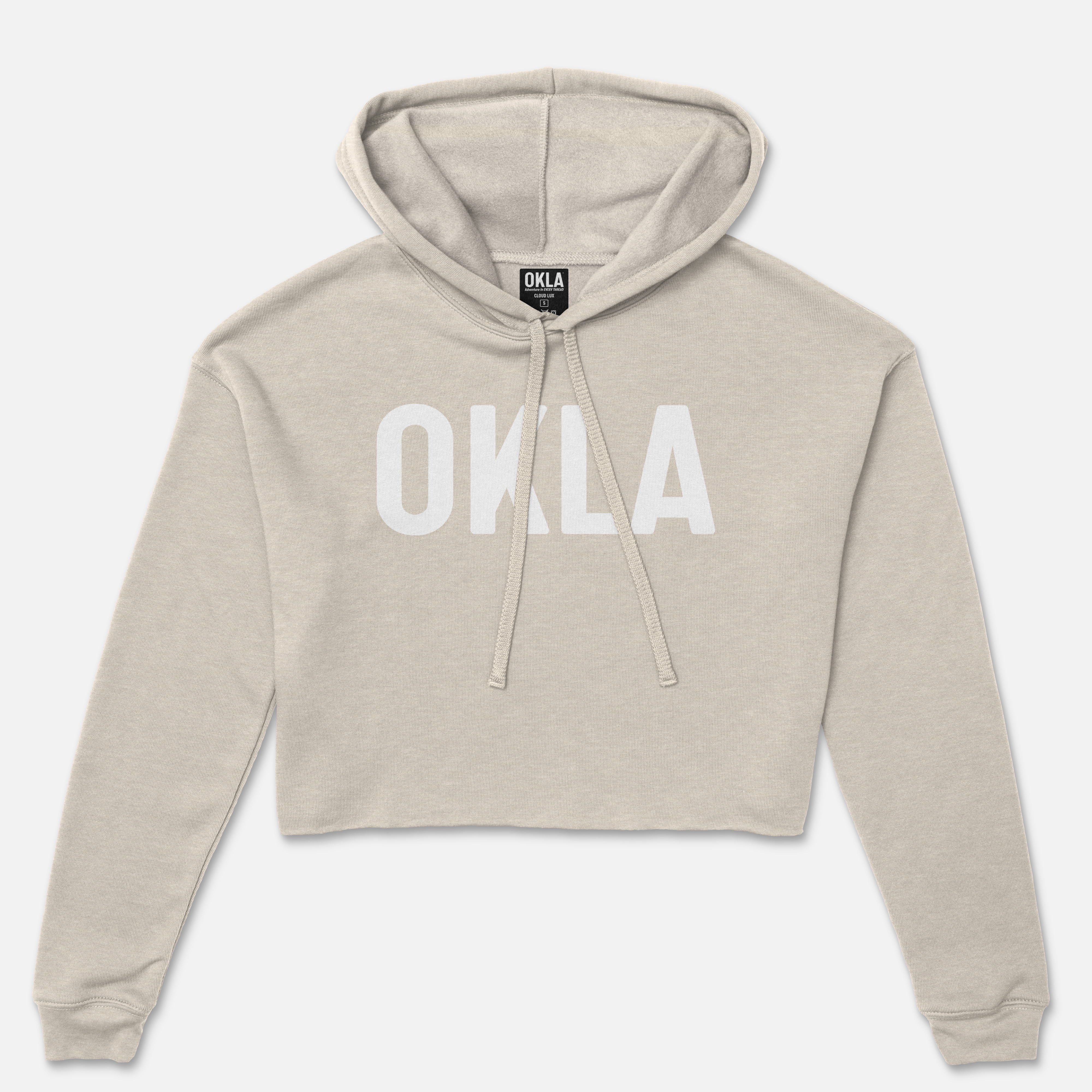 The OKLA Original Crop Hoodie, worthy of a fashion magazine, showcases long sleeves and a cozy fleece texture in a chic beige color. Its trendy design features a front pouch pocket and "OKLA" boldly printed in white across the chest, complemented by a functional drawstring hood.