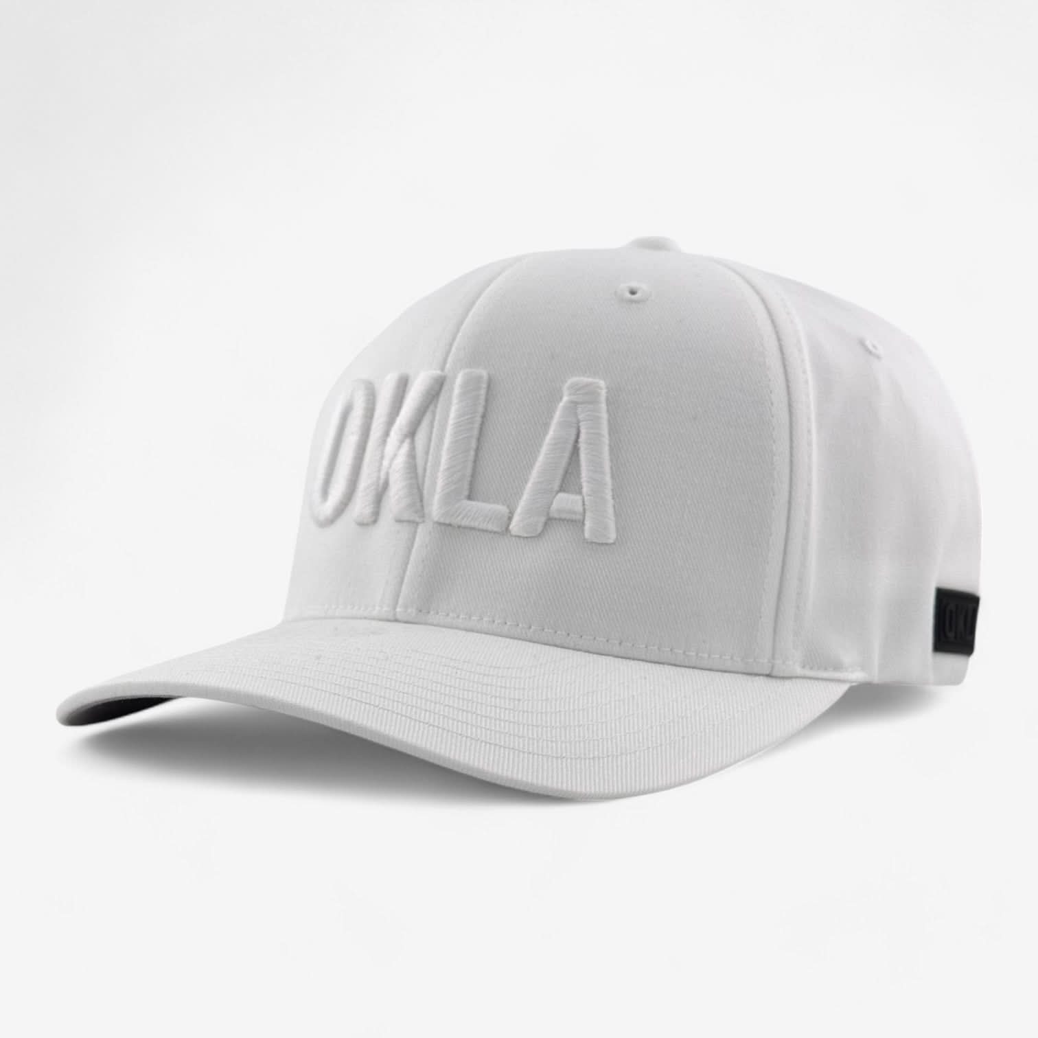 Introducing the OKLA Original White Embroidered hat, a fashionable cap that showcases 'OKLA' in bold letters on the front. Designed with an athletic shape and a curved brim, this stylish hat also features a black tag on the side and an elastic stretch band for enhanced comfort.