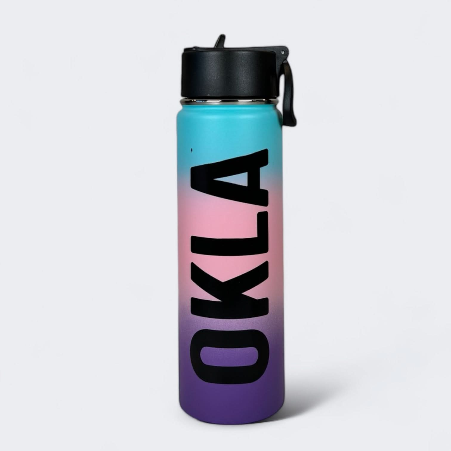 The OKLA - Travel Thermos 22oz features a striking blue to purple gradient design with "OKLA" prominently printed in large black letters. It boasts a secure black leak-proof lid and a handy small handle, all set against a plain light grey background.