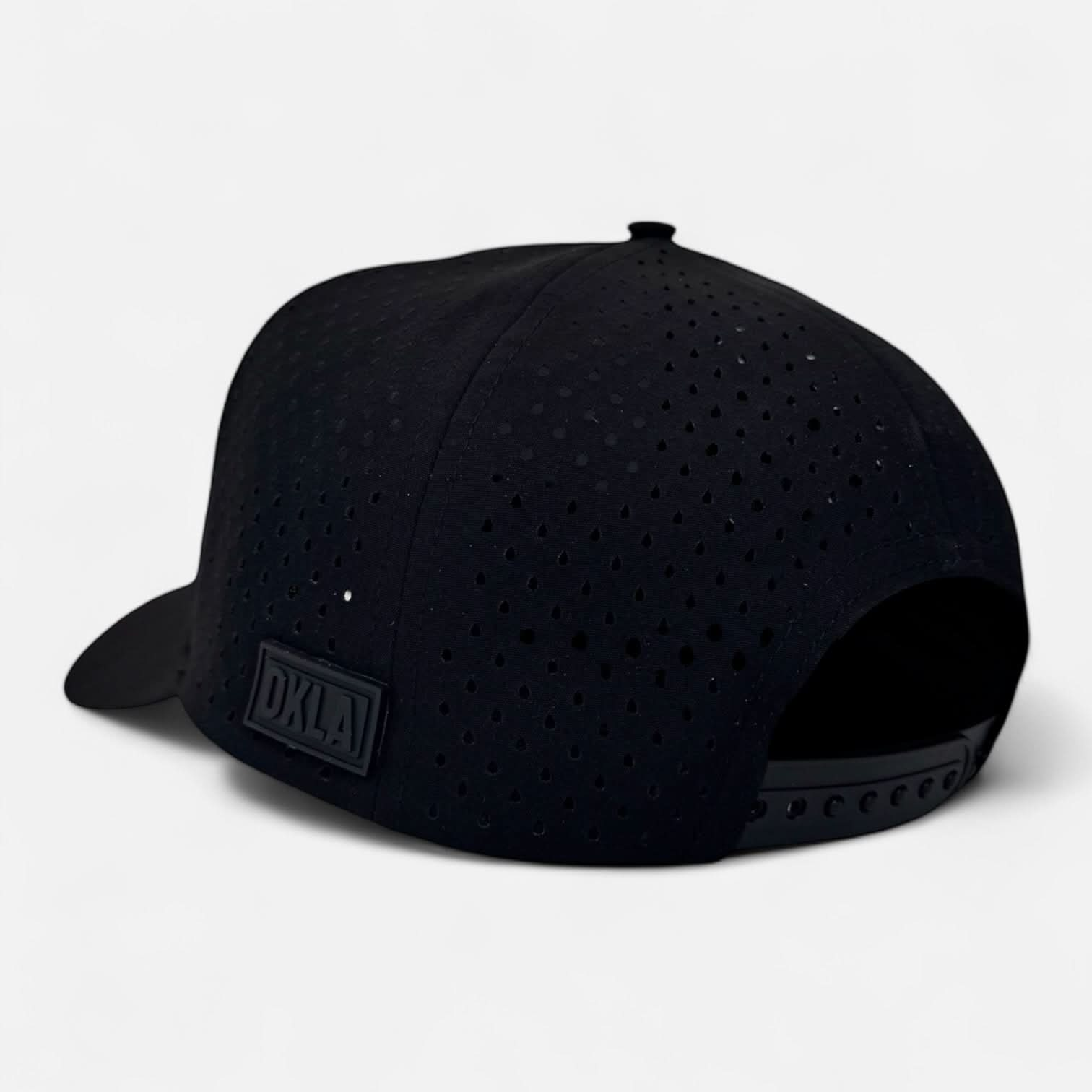 The OKLA Navigator Hat is displayed from the back, showcasing its black snapback design with a perforated pattern. It includes an adjustable strap, a vintage-inspired 3D patch, and a stitched label in capital letters reading 'DKLA'. Equipped with sweat-wicking technology, the cap is set against a plain white background.