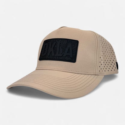 The OKLA Navigator Hat is a beige baseball cap with a vintage-inspired 3D patch on the front, featuring intricate patterns. Designed for comfort, it incorporates ventilation holes and sweat-wicking technology to keep you cool on sunny days.