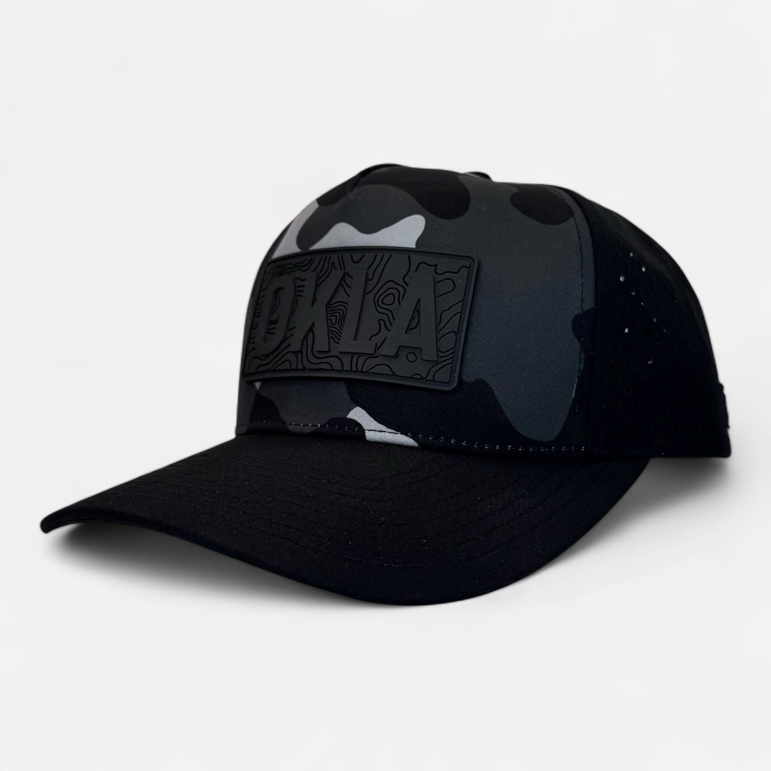 The OKLA Navigator Hat is a camouflage-patterned baseball cap with a flat brim, featuring a vintage-inspired 3D black patch on the front. The patch showcases embossed text against a plain white background.