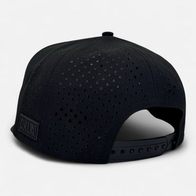 Introducing the OKLA Navigator Hat: a black baseball cap with a perforated design and sweat-wicking technology. It features an adjustable strap at the back and is adorned with a small DXLA label set against a plain white background.
