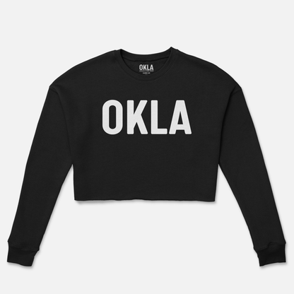 The OKLA Original Crop Sweatshirt is a black, long-sleeve cropped sweatshirt made from soft fleece, featuring the letters "OKLA" prominently printed in white on the front. Ideal for achieving those fashion magazine-inspired street styles.