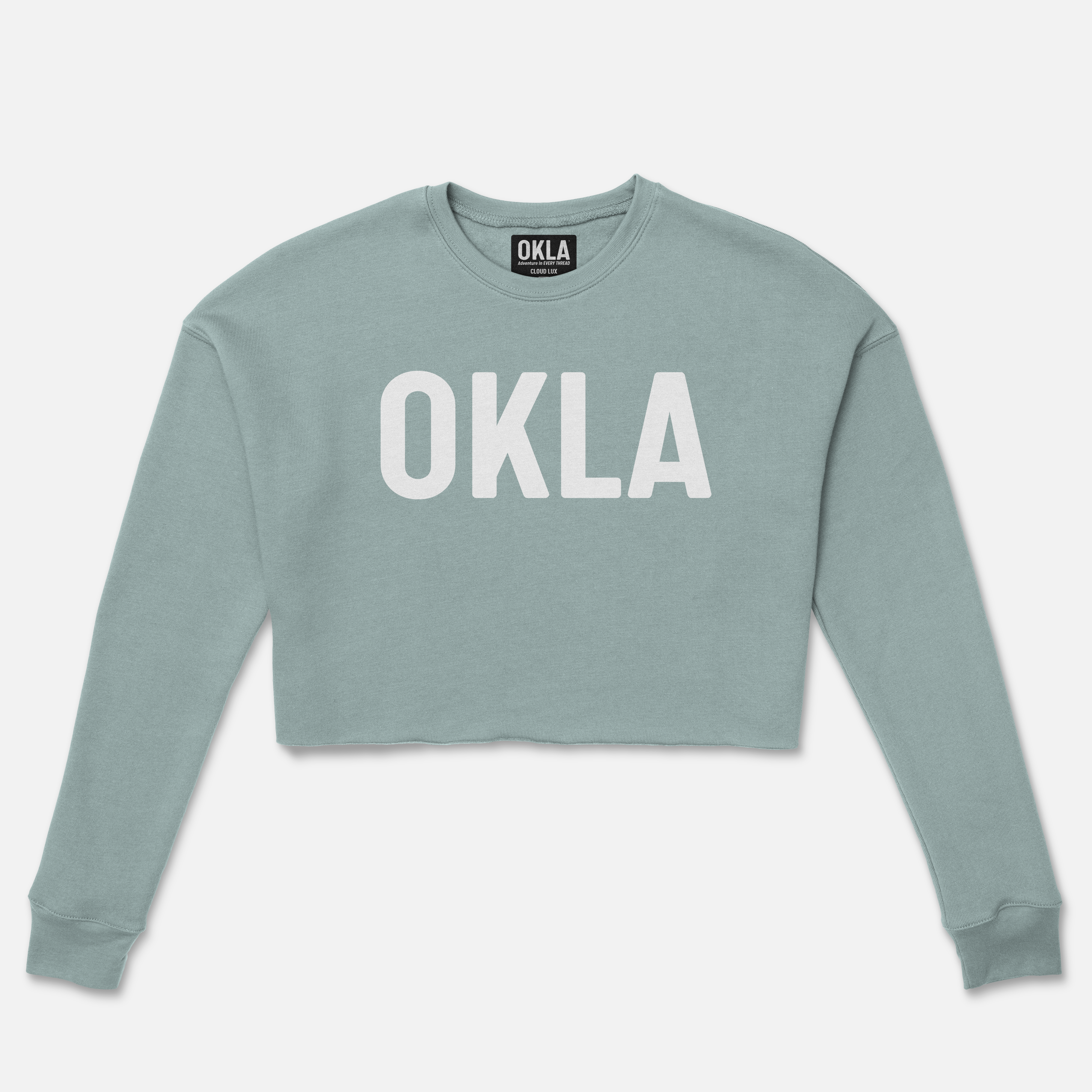 The OKLA Original Crop Sweatshirt is a long-sleeve, light blue fleece top featuring "OKLA" in bold white capital letters. Its simple yet trendy design with ribbed cuffs makes it perfect for making a fashion-forward statement.