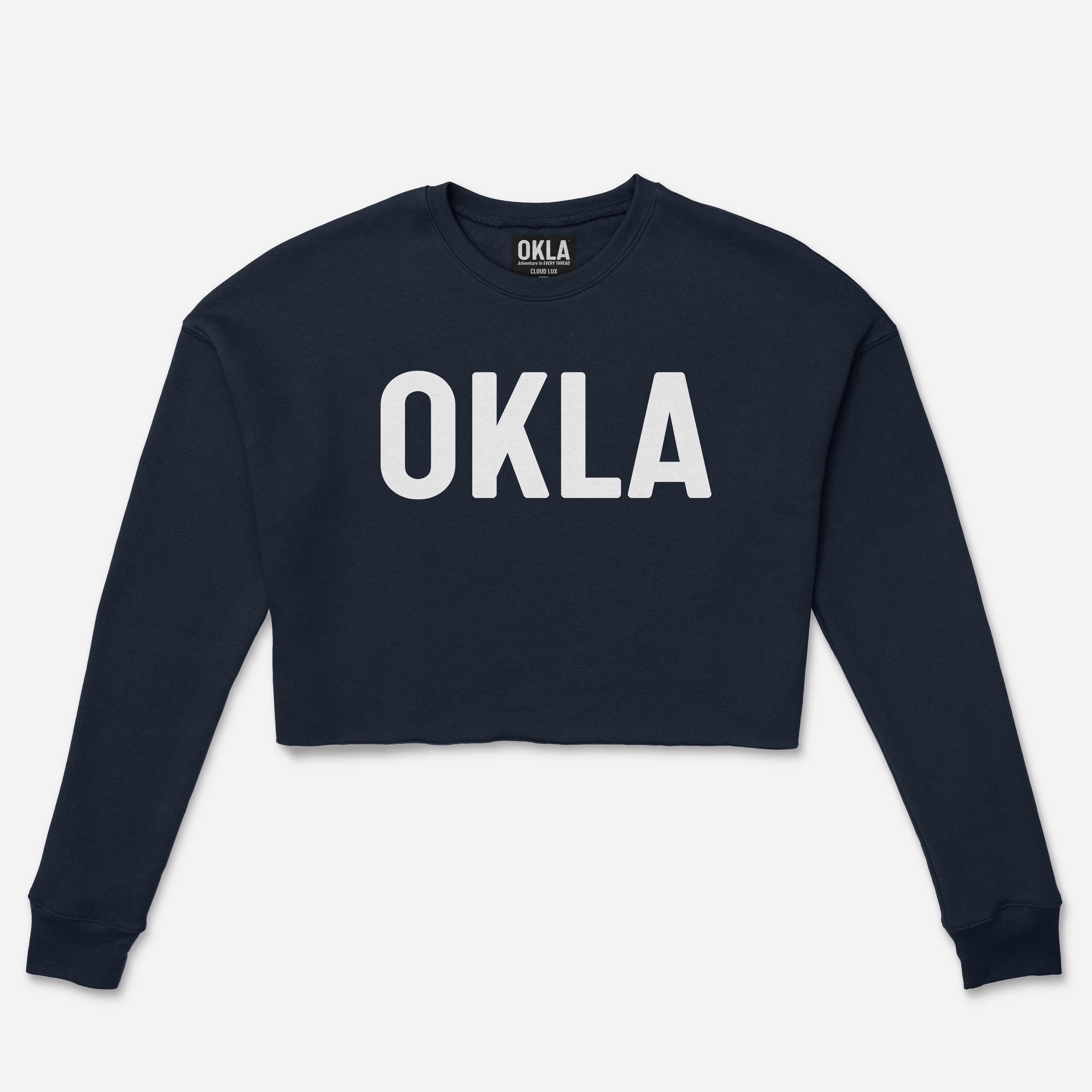 The OKLA Original Crop Sweatshirt, featuring a navy blue fleece design and the word "OKLA" printed in white uppercase letters on the front, is the perfect addition for a casual feature in any fashion magazine. It is presented laid flat against a plain white background.