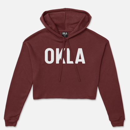 The OKLA Original Crop Hoodie features a maroon fleece design with the word "OKLA" prominently displayed in large white letters on the front. Complete with a drawstring hood and long sleeves, it offers a stylish look reminiscent of high-fashion magazine spreads.