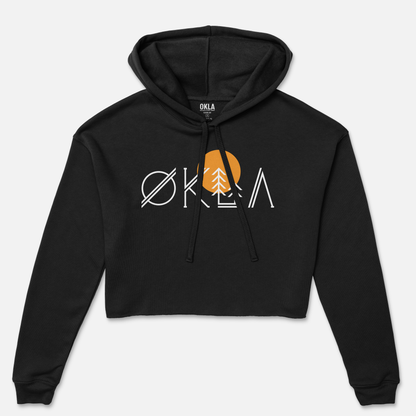 Introducing the OKLA Native Crop Hoodie: a black fleece crop hoodie showcasing a minimalist design with the word "OKLA" in white. The letter "A" features a unique tree stylization, complemented by a large orange circle behind it, reminiscent of a sun. Ideal for making fashion-forward statements, this hoodie is equipped with a drawstring and front pocket.