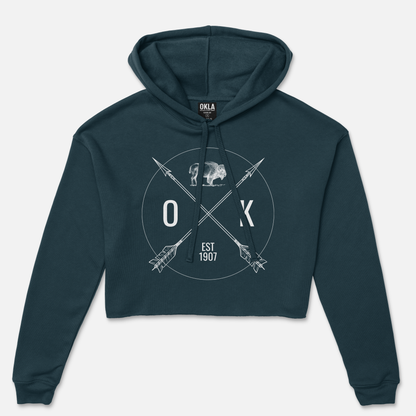 The OKLA Shield - Crop Hoodie combines fashion-forward style and comfort, featuring a chic dark teal design with crossed arrows, the text "OKLA," "Est 1907," and a buffalo silhouette. Constructed from soft fleece, it also includes the OKLA label inside the hood for an extra touch of style.