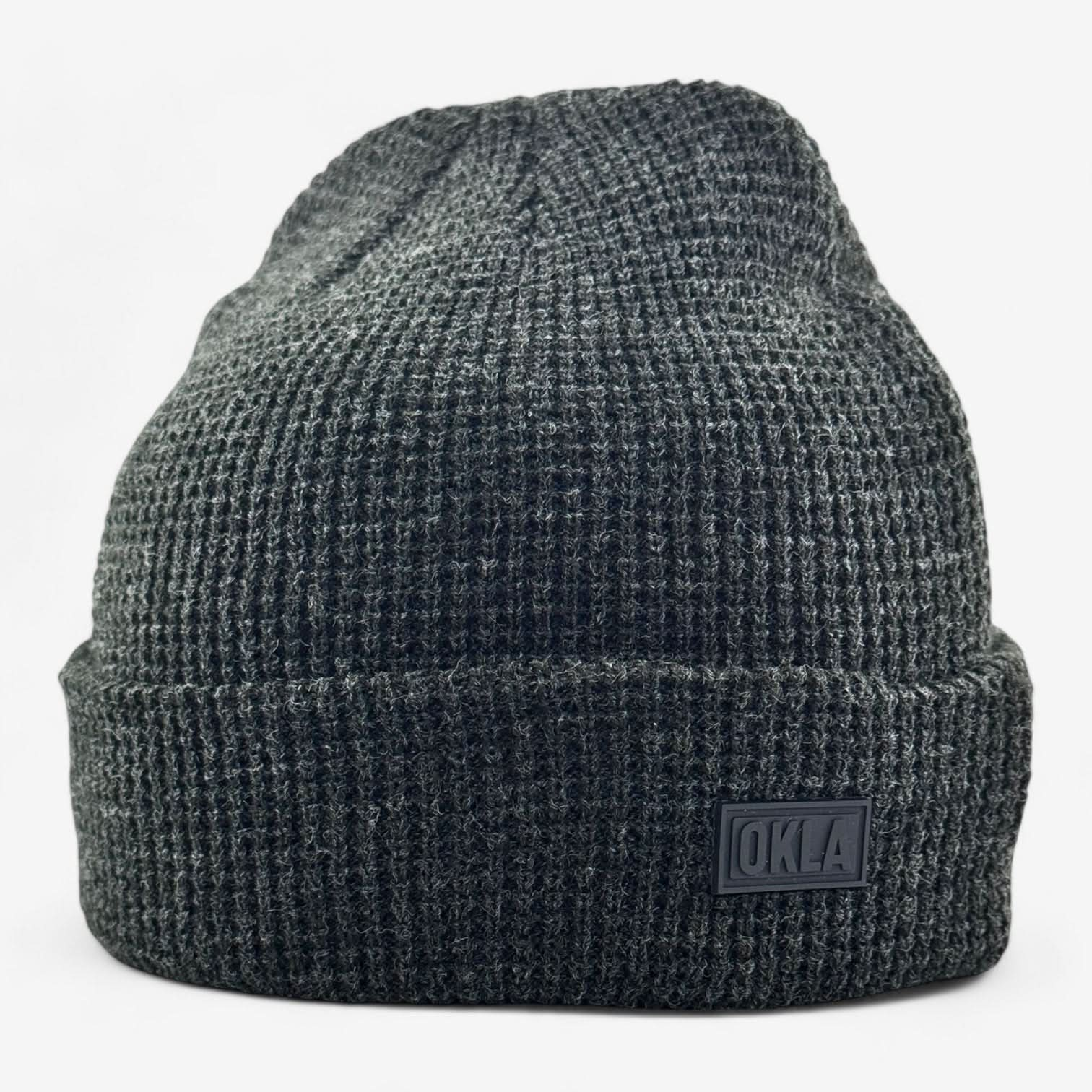 The OKLA Modern Beanie is a dark gray knitted waffle knit cuff beanie with a folded brim, featuring a small rectangular rubber OKLA seal on the front. Its thick and warm texture makes it ideal for cold weather.