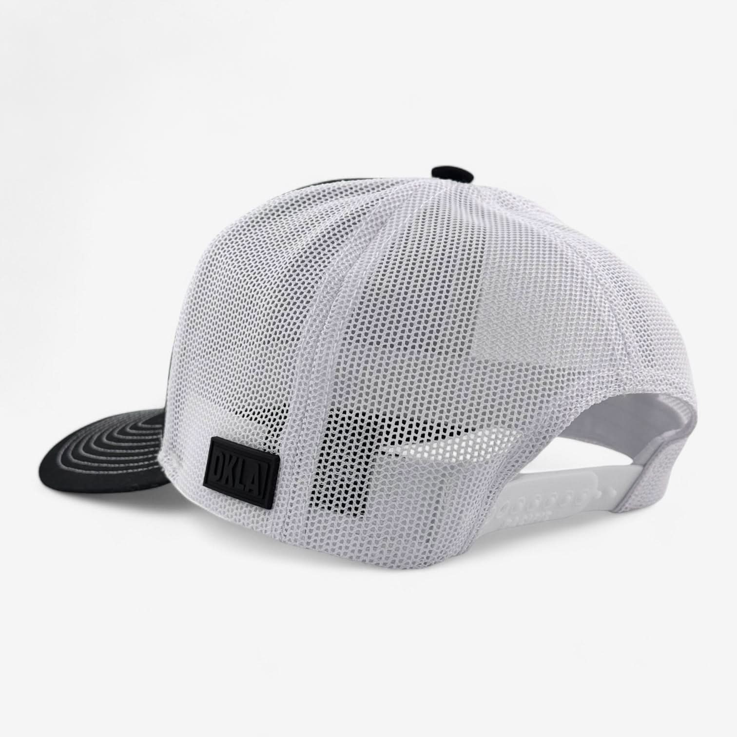 The OKLA Legacy Trucker Hat, made with high-quality mesh material, displays a retro-style PVC patch. This black and white hat includes a curved brim and has an adjustable snapback closure visible from the back.