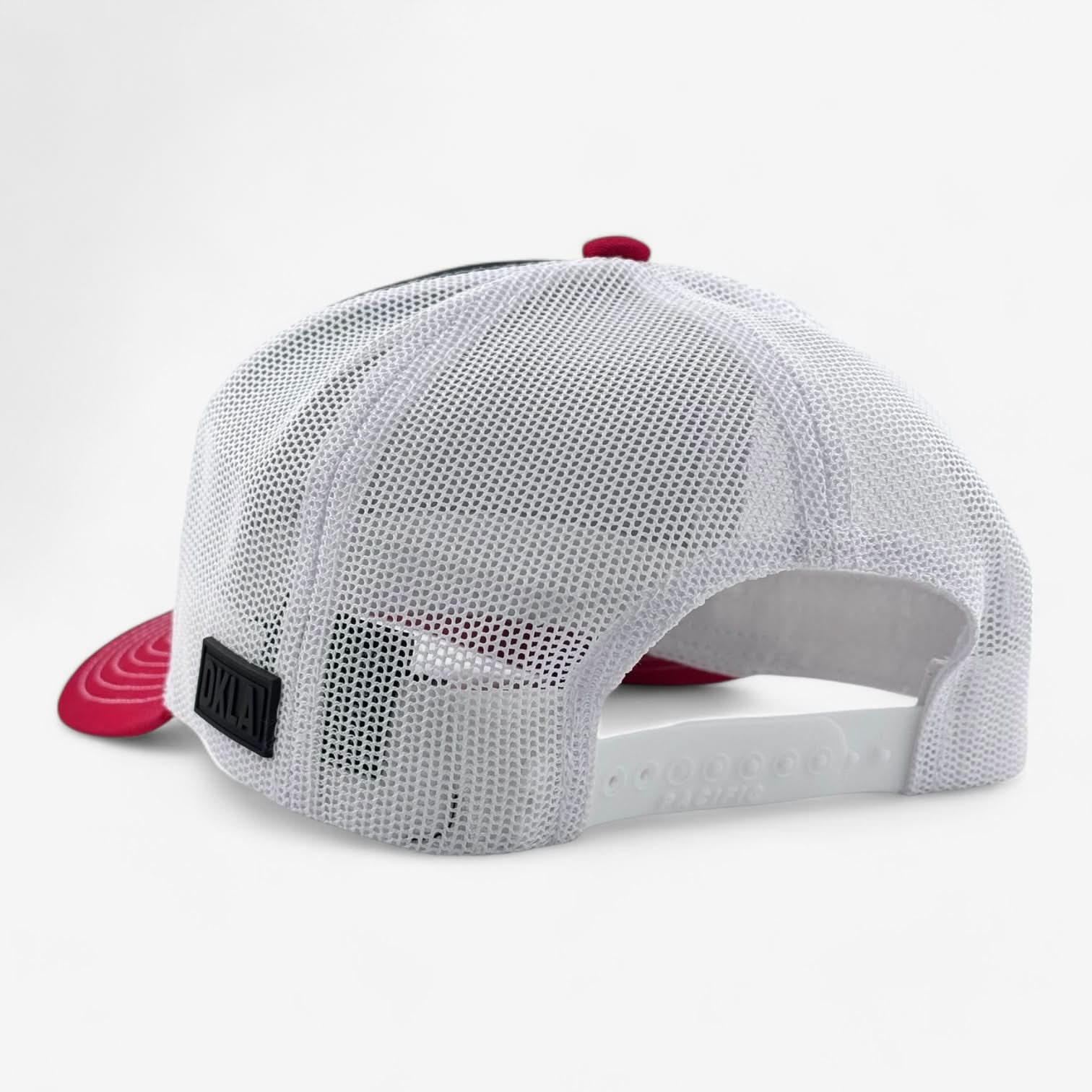 From the rear view, a red and white OKLA Legacy Trucker Hat is displayed, featuring a snapback closure and crafted from premium mesh fabric. The cap includes a vintage-inspired PVC patch on the side with white text, capturing its classic charm.