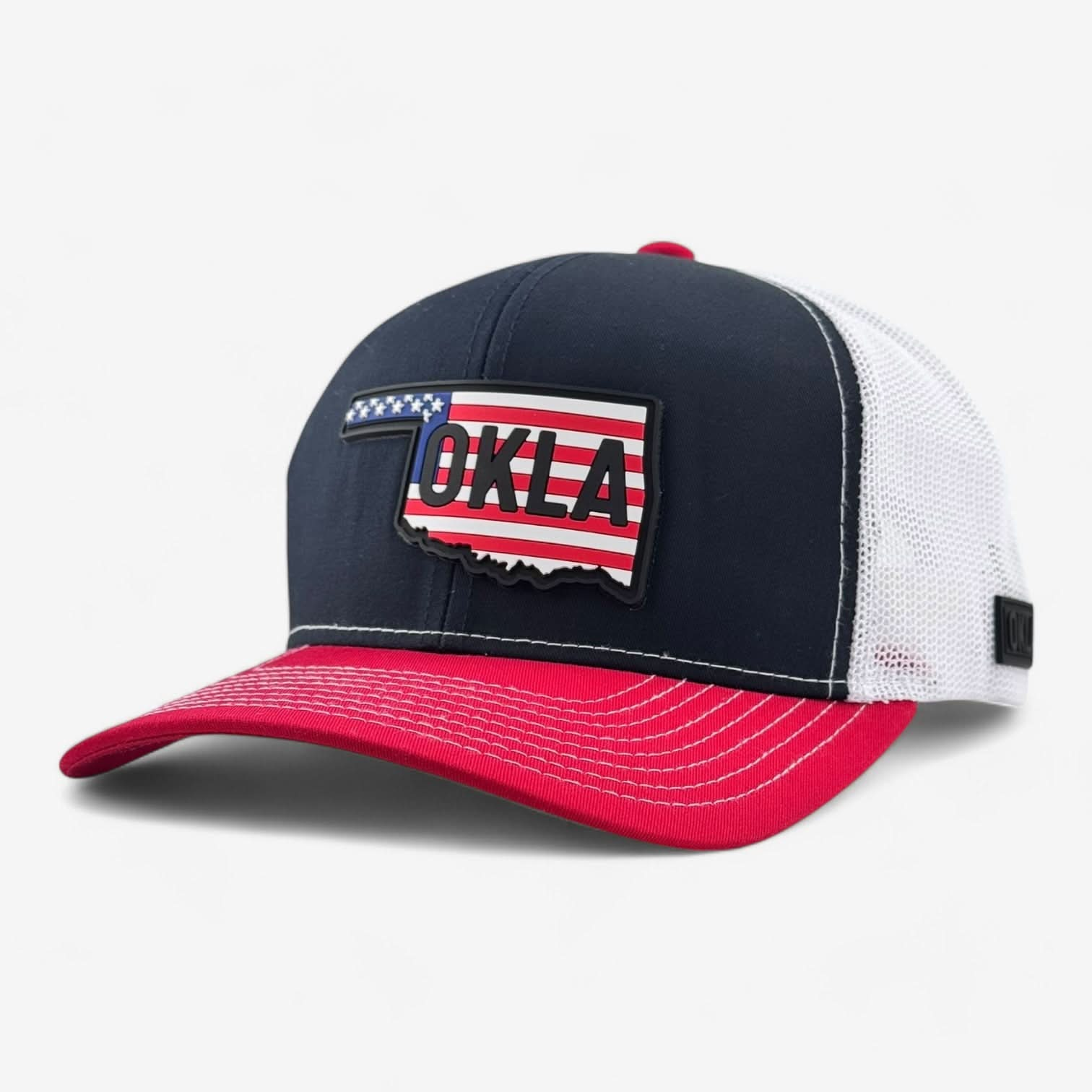 The OKLA Legacy Trucker Hat features a vintage-inspired PVC patch on the front, with a combination of red, white, and blue colors. Made from premium mesh fabric, it displays an American flag pattern outlining Oklahoma and bold "OKLA" letters, offering both comfort and patriotic style to your outfit.