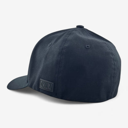 The OKLA Original Fitted Hat is displayed from the back, highlighting the logo OKLA in subtle dark lettering. This black baseball cap features an elastic stretch band for comfort and a curved brim, all set against a plain white background.