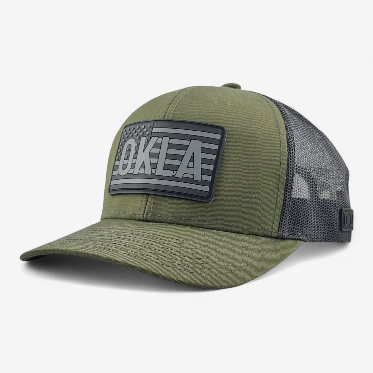 Introducing the OKLA Freedom Trucker Hat, a vintage-style military green baseball cap with a black mesh back and a 3D patch. The patch prominently showcases an American flag with the letters OKLA, all designed with sweat-wicking technology for maximum comfort.