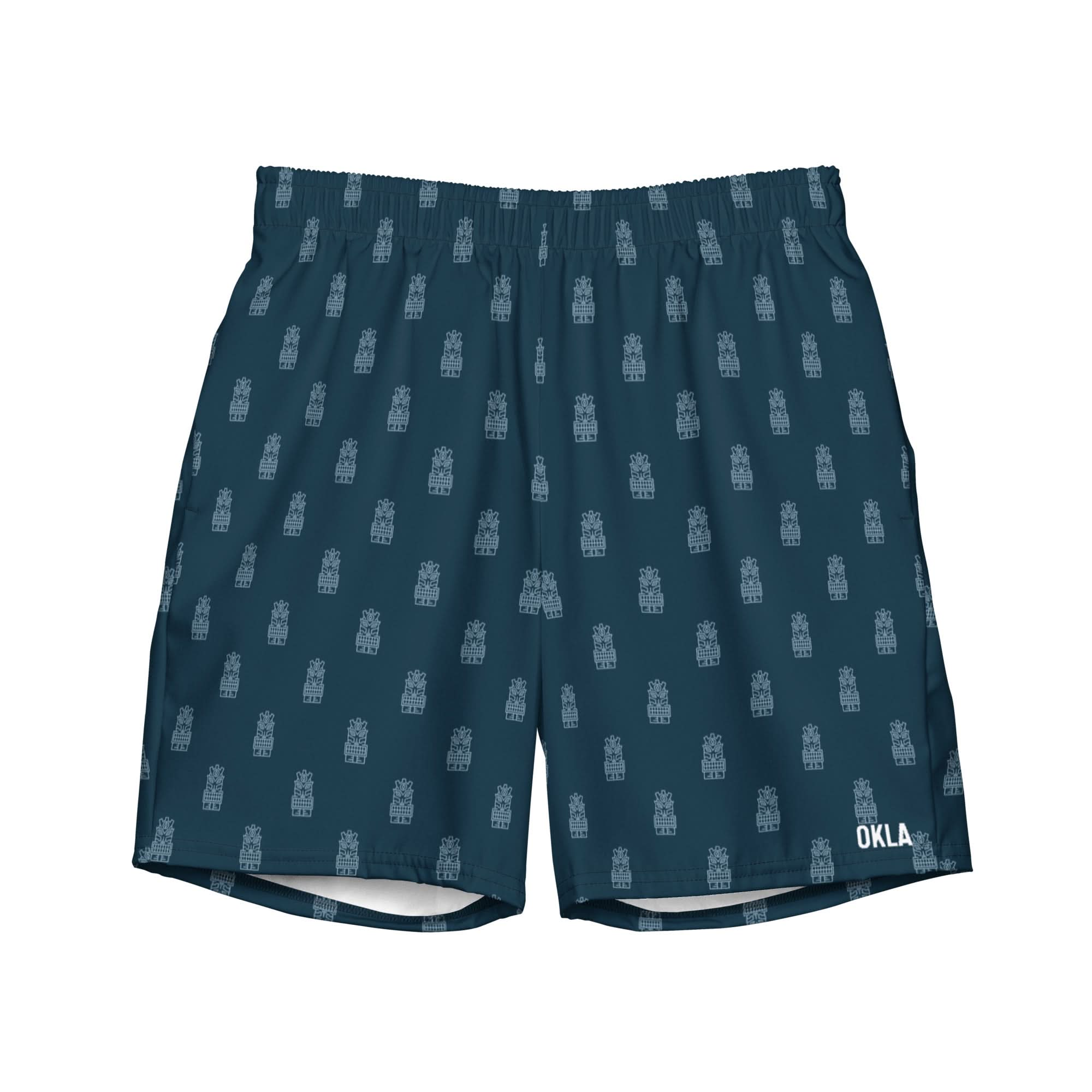 Tiki Boardshorts are blue athletic shorts featuring a drawstring waistband and crafted from quick-dry fabric with a repeating pattern of small, intricate designs. The word "OKLA" is printed at the bottom-right corner for an added touch of style.