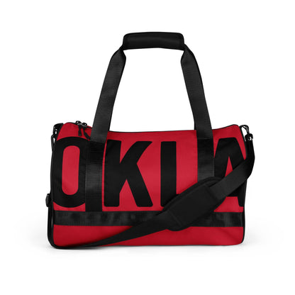 The OKLA - Gym Bag Red Series is a durable red duffle gym bag with black handles and straps, prominently displaying bold black letters spelling OKLA on its side.