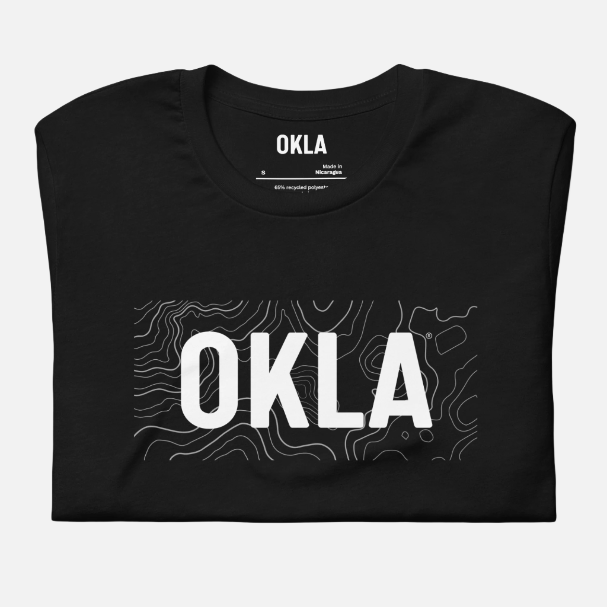 The OKLA Navigator Tee, made from recycled cotton, is a black T-shirt that perfectly combines adventure and comfort. It features large white lettering and a subtle contour line pattern in the background for an understated, eco-friendly look.