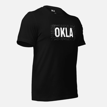 The OKLA Navigator Tee is a black T-shirt made from recycled cotton, showcasing the word OKLA in bold white letters complemented by a subtle wavy line pattern. Perfect for adventure seekers who value comfort, it's attractively presented on a crisp white backdrop.