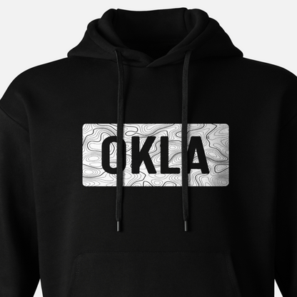 The OKLA Navigator BOLD Hoodie is designed for both exploration and ease, showcasing a black color scheme with a white rectangular center that presents prominent OKLA lettering atop a nuanced topographic backdrop. Constructed entirely from recycled cotton, this hoodie includes a drawstring hood and front pocket.