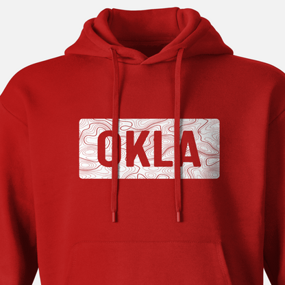 The OKLA Navigator BOLD Hoodie is a red hoodie crafted from recycled cotton. It features a drawstring hood and prominently displays a white rectangular patch on the front, showcasing OKLA in vibrant red over a subtle wavy line pattern, designed for both adventure and comfort.